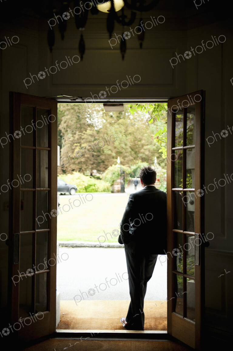 Silhouette of a man standing in a doorway leaning against the door frame, looking out…