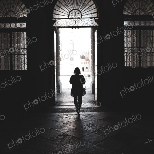 Silhouette of a woman walking through an arched doorway in Venice, Veneto, Italy.