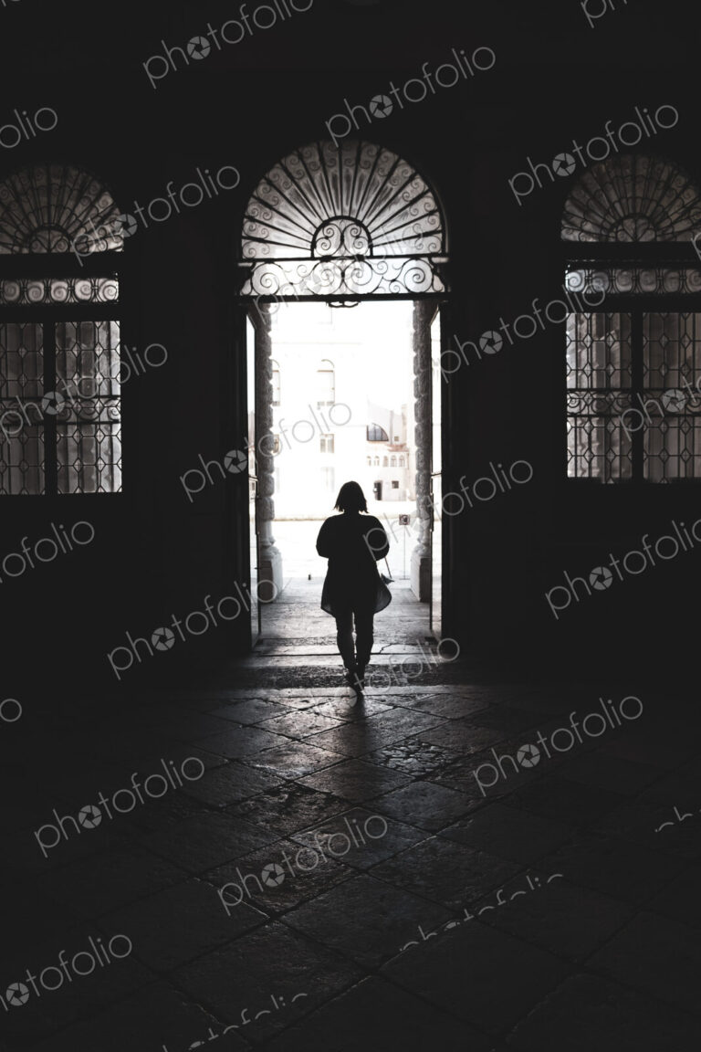 Silhouette of a woman walking through an arched doorway in Venice, Veneto, Italy.