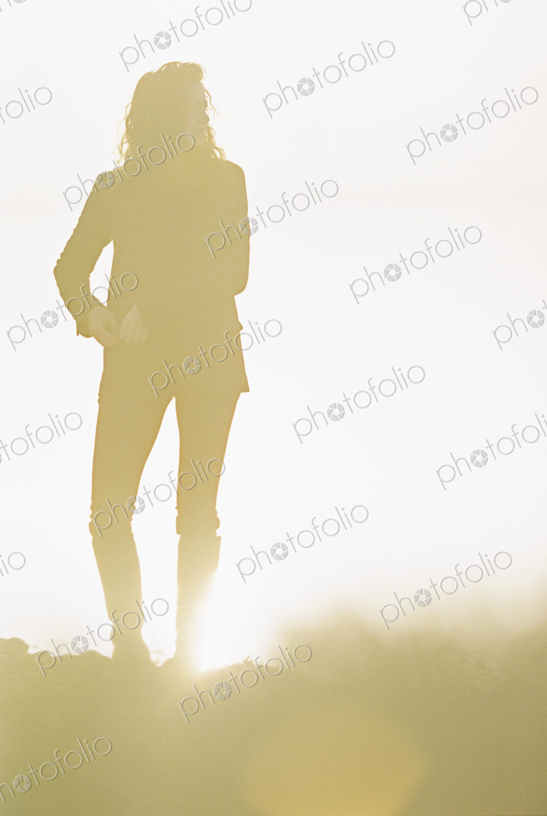 Silhouette of a woman with long curly hair standing in a sunlit landscape.
