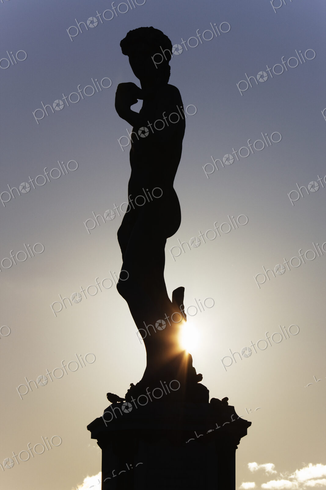 Silhouette of classical statue with setting sun behind.