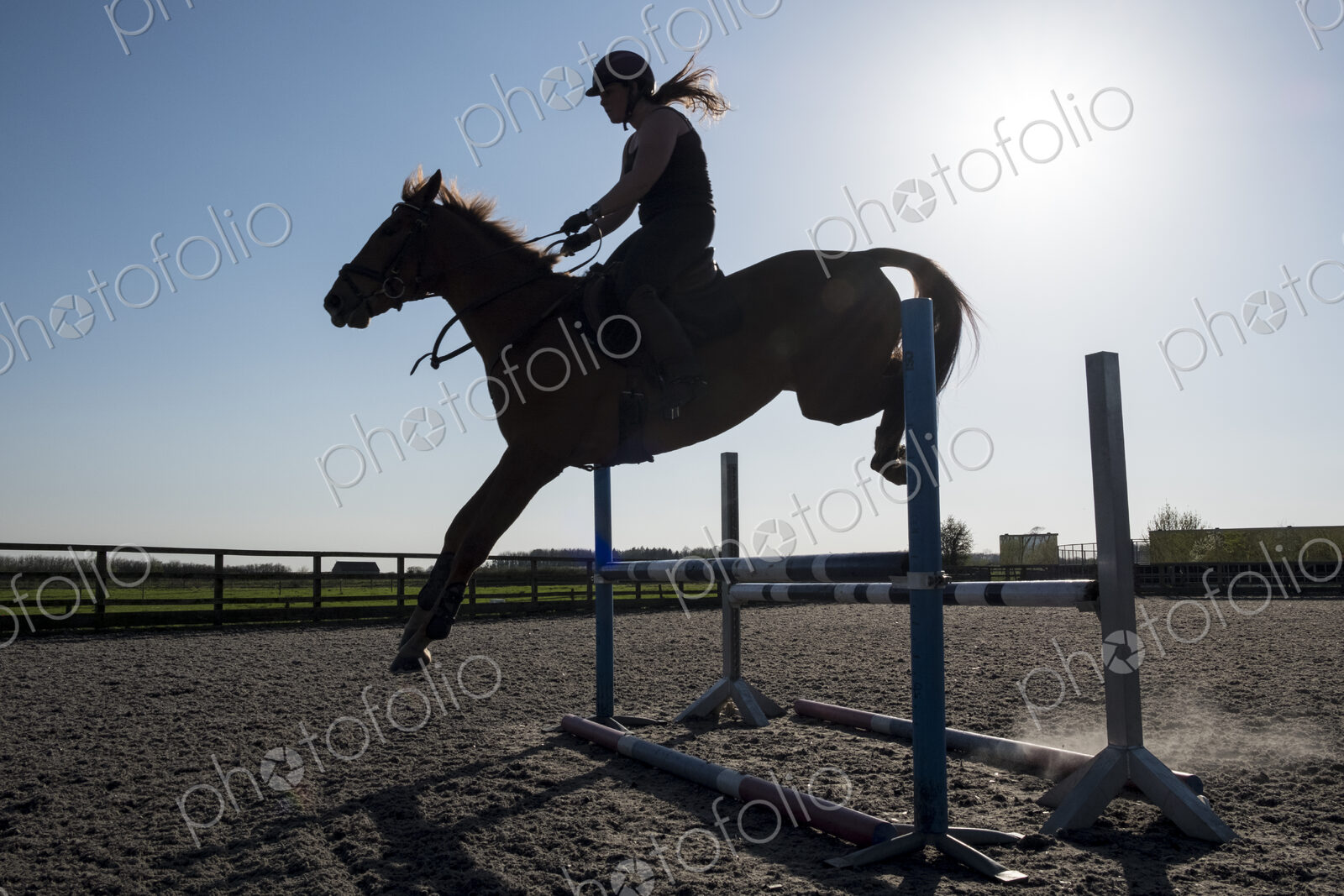 Silhouette of female rider jumping a hurdle on a showjumper horse.