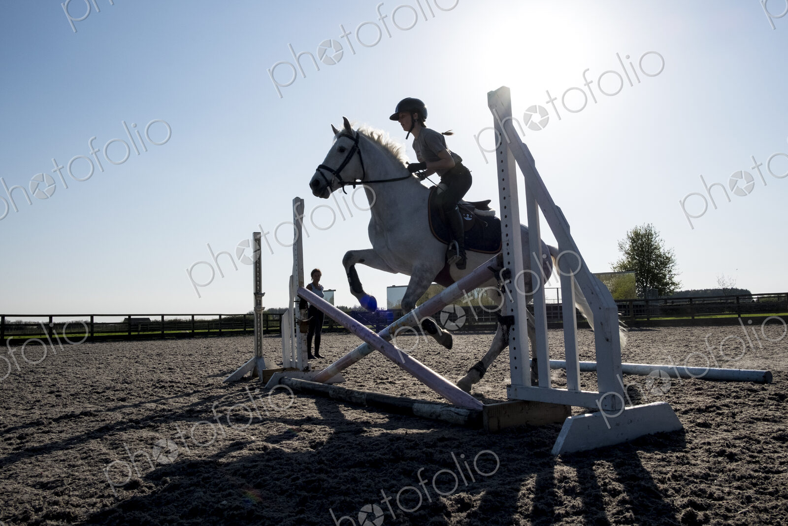 Silhouette of female rider jumping hurdle in a paddock on a grey horse