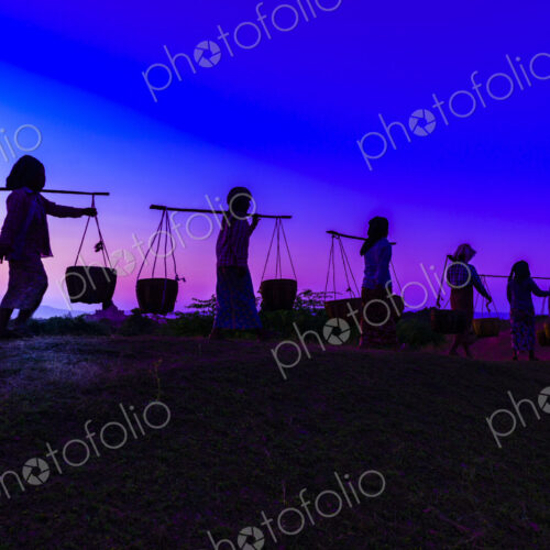 Silhouette of people carrying baskets under sunset sky
