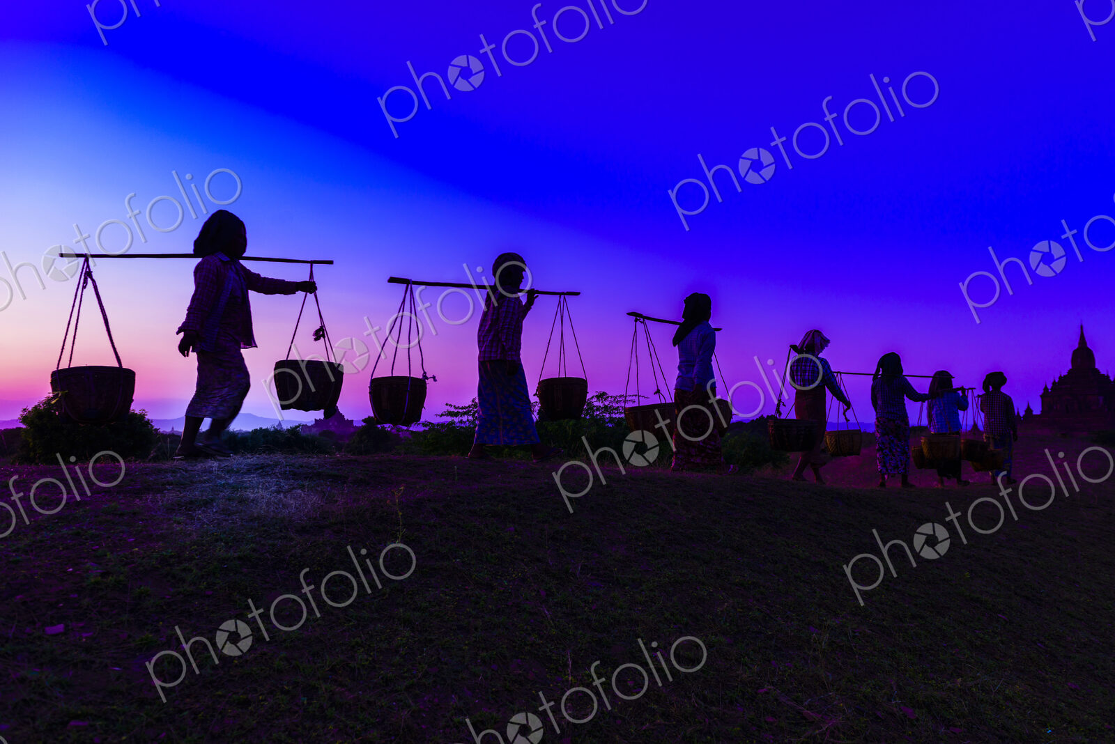 Silhouette of people carrying baskets under sunset sky