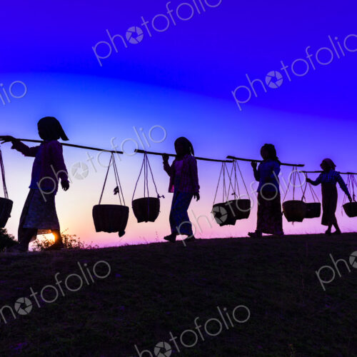 Silhouette of people carrying baskets under sunset sky