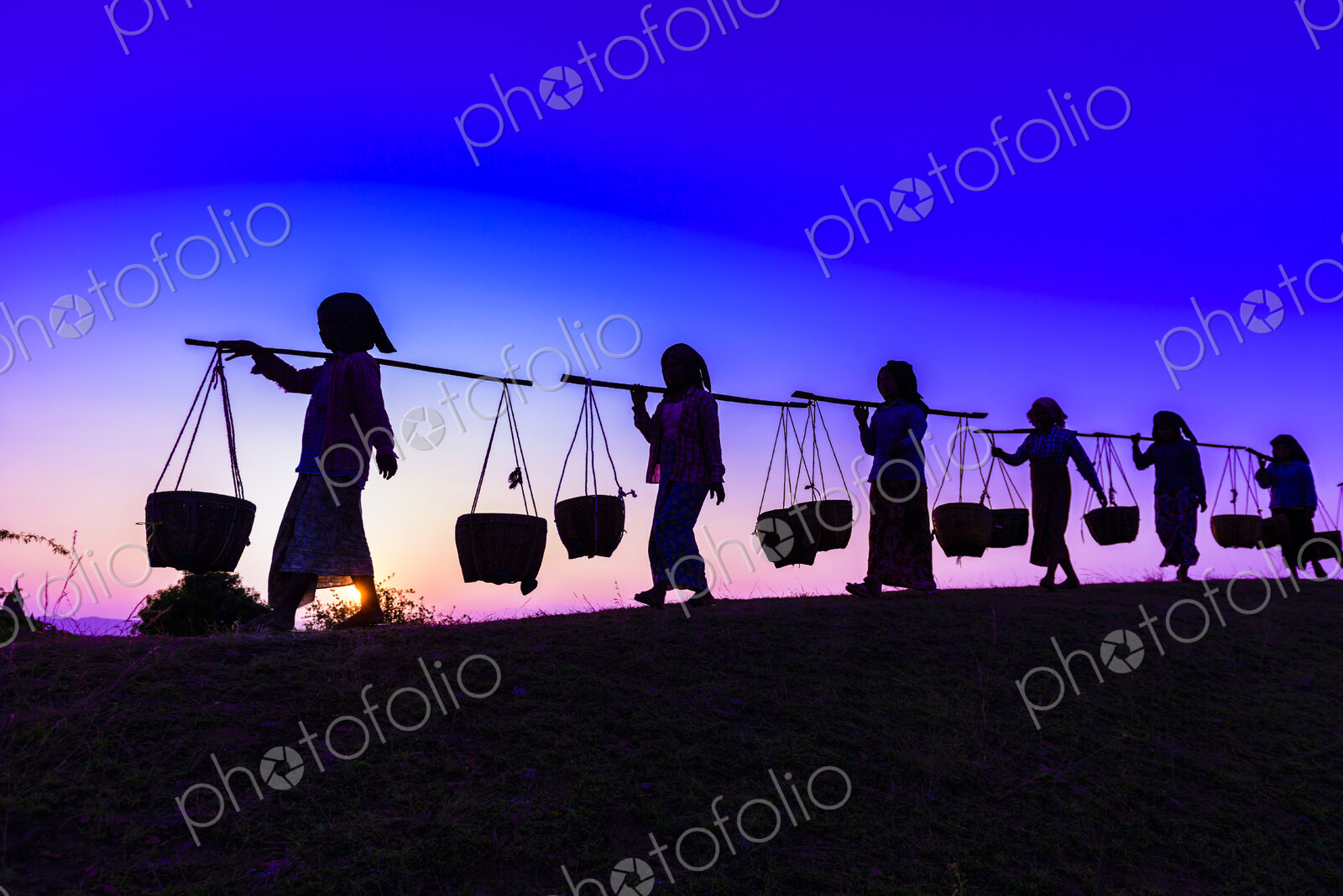 Silhouette of people carrying baskets under sunset sky