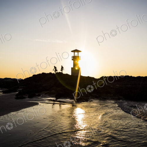 Silhouette of two people walking past lighthouse by the ocean at sunset. Silhouette of two people walking past lighthouse by the ocean at sunset.