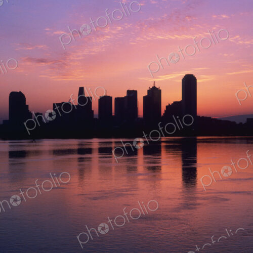 Silhouettes of skyscrapers at dawn with lake in foreground.