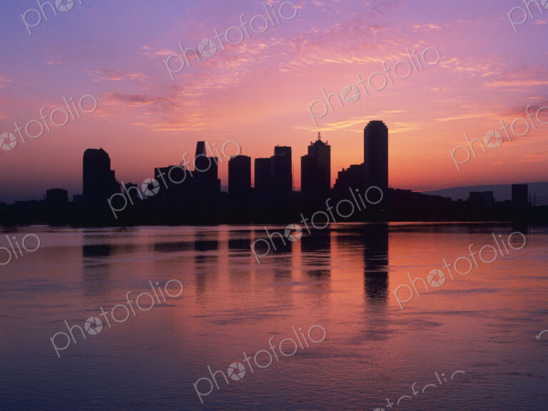 Silhouettes of skyscrapers at dawn with lake in foreground.