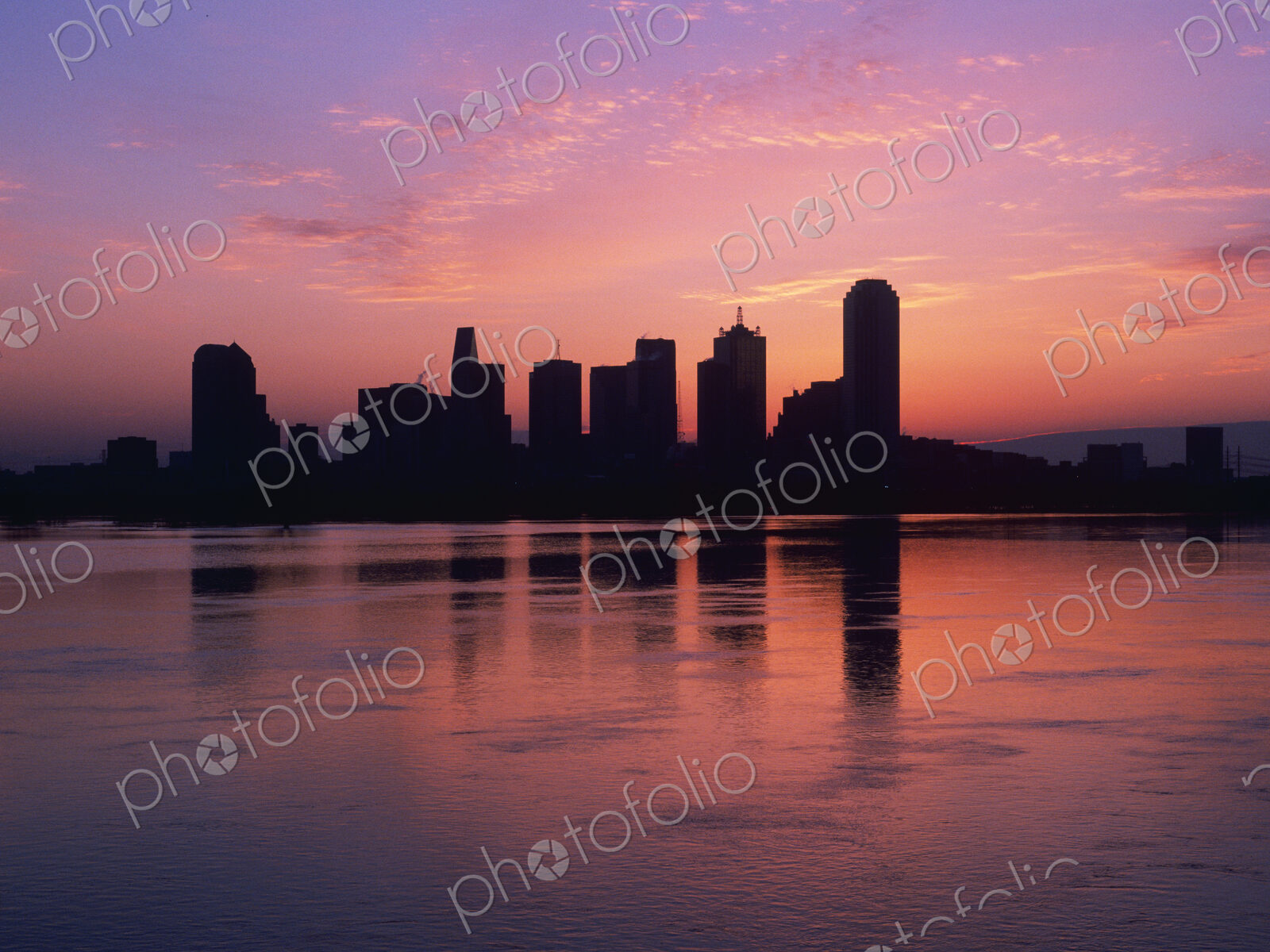 Silhouettes of skyscrapers at dawn with lake in foreground.