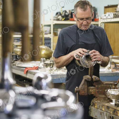 Silversmith restoring silver cup in workshop. Silversmith restoring silver cup in workshop.