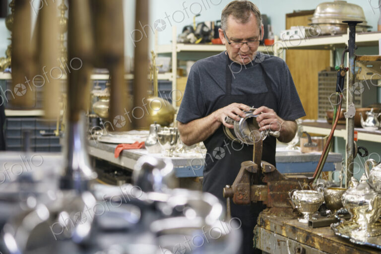 Silversmith restoring silver cup in workshop.
