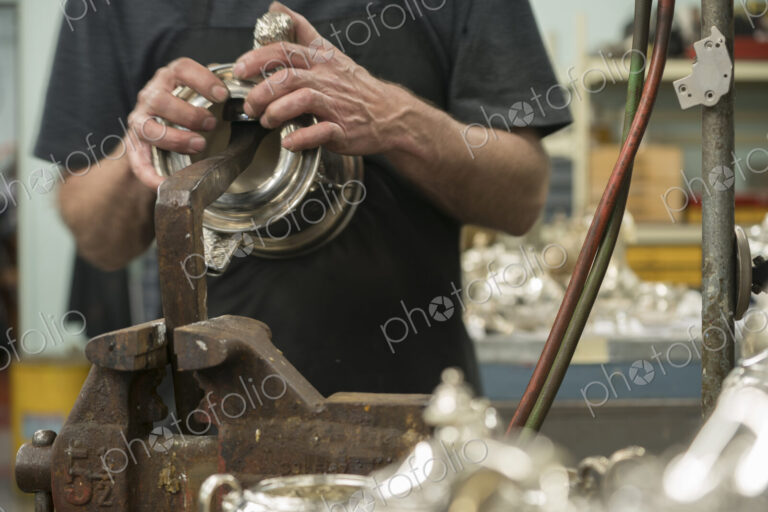 Silversmith restoring silver cup in workshop.