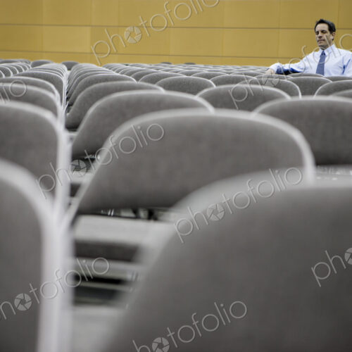 Single businessman sitting in a room full of chairs prior to a conference centre meeting. Single businessman sitting in a room full of chairs prior to a conference centre meeting.