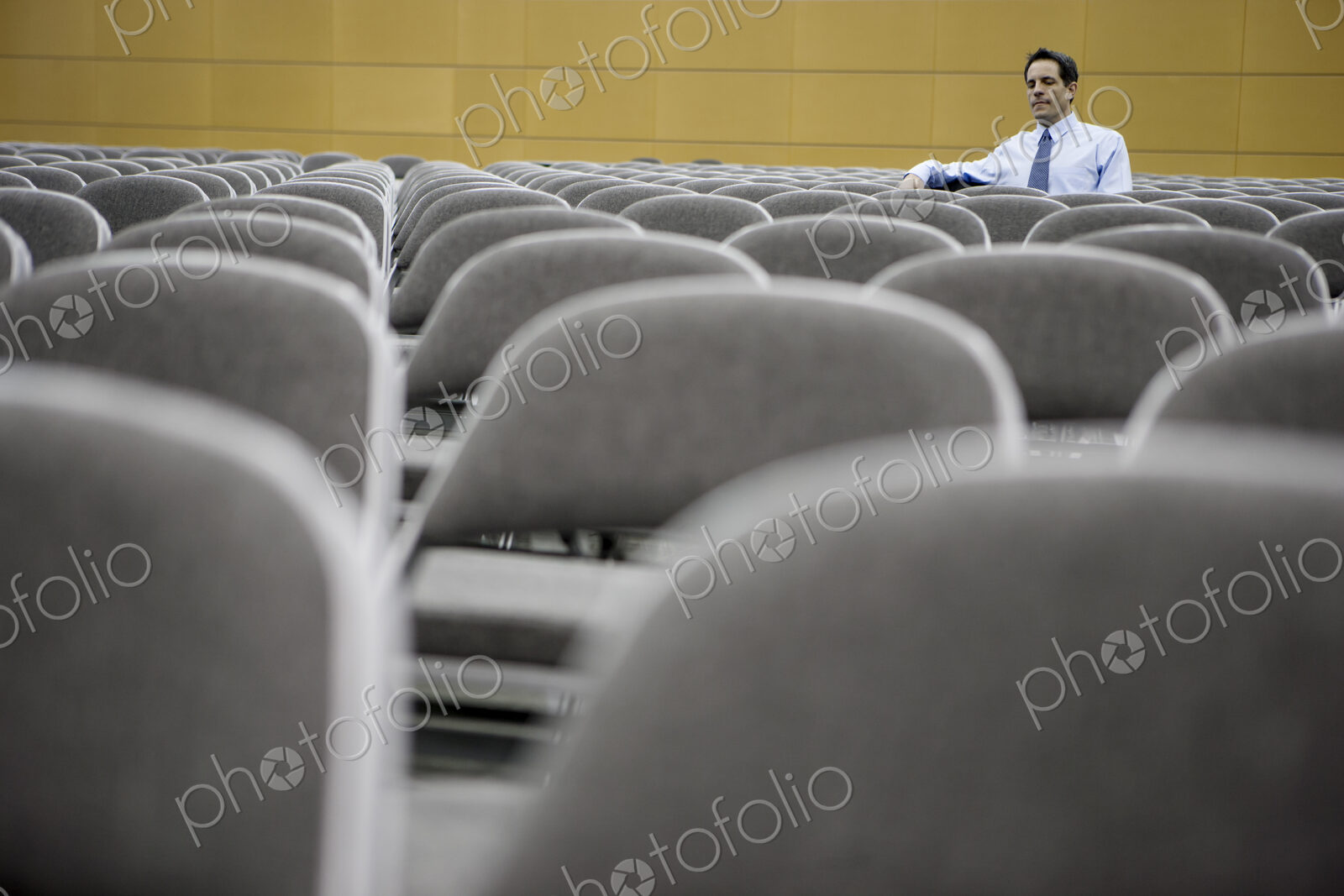 Single businessman sitting in a room full of chairs prior to a conference centre meeting.
