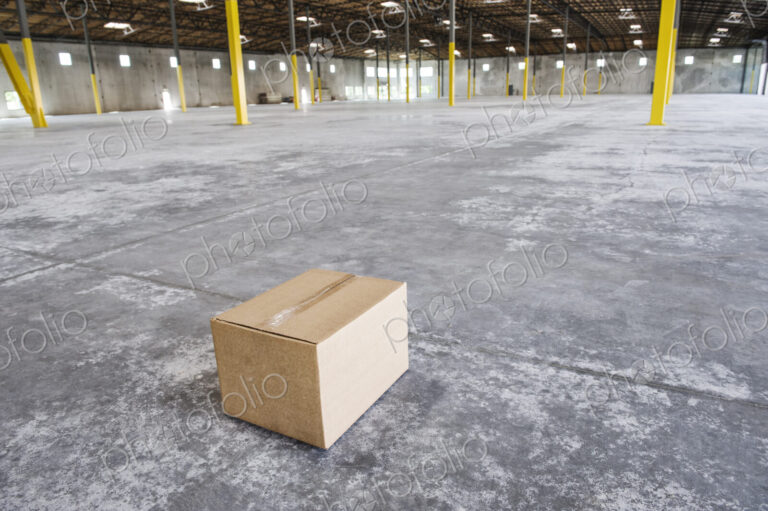 Single cardboard box in the middle of a new empty warehouse space.