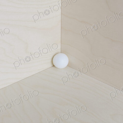 Single white ball in corner of a wooden box.