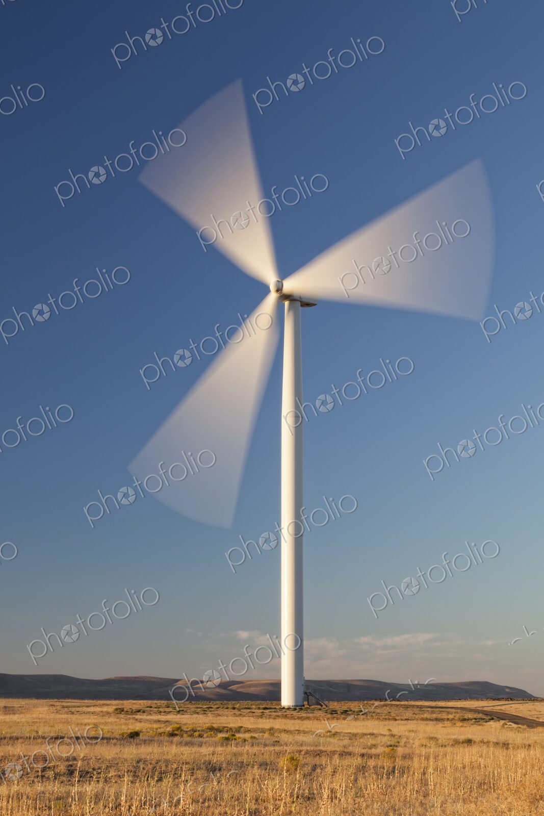 Single wind turbine spins in an open Oregon field beneath a clear blue sky,…