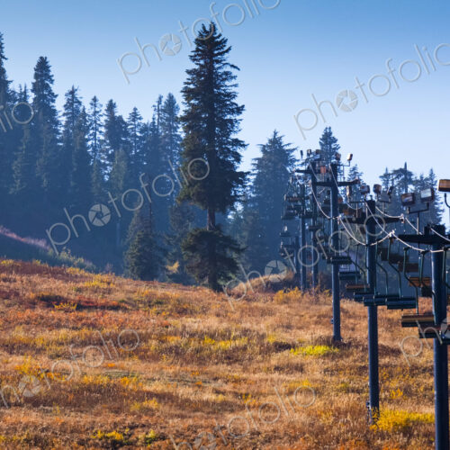 Ski lift chairs in summer on the slopes of the pass, pine trees and brown grass.