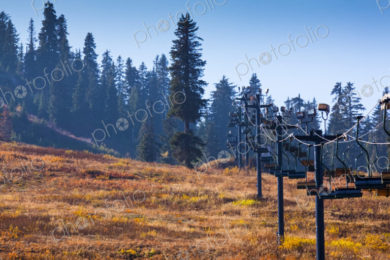 Ski lift chairs in summer on the slopes of the pass, pine trees and brown grass.