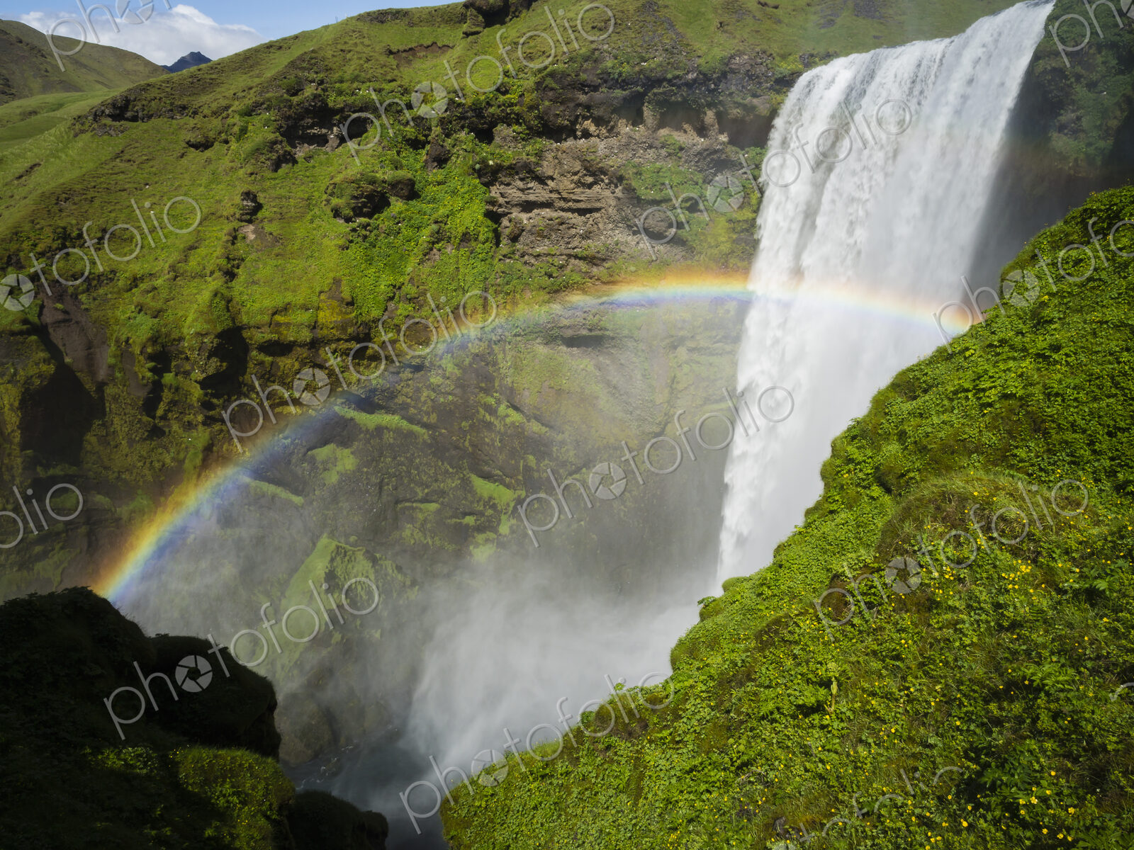 Skogafoss waterfall, a cascade over a sheer cliff, and a rainbow in the mist.