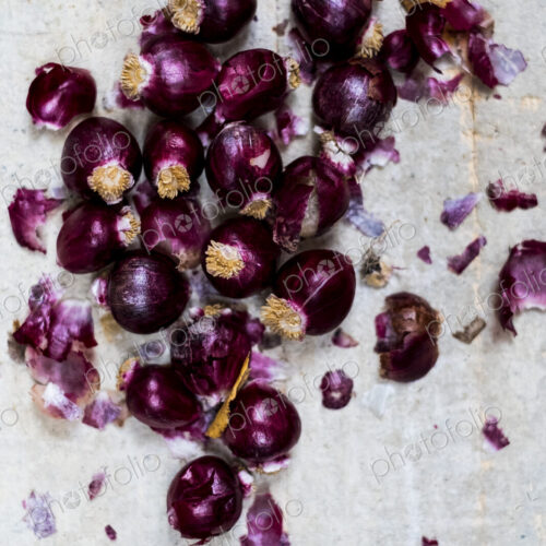 Small glossy red onions and papery outer skins on grey background.