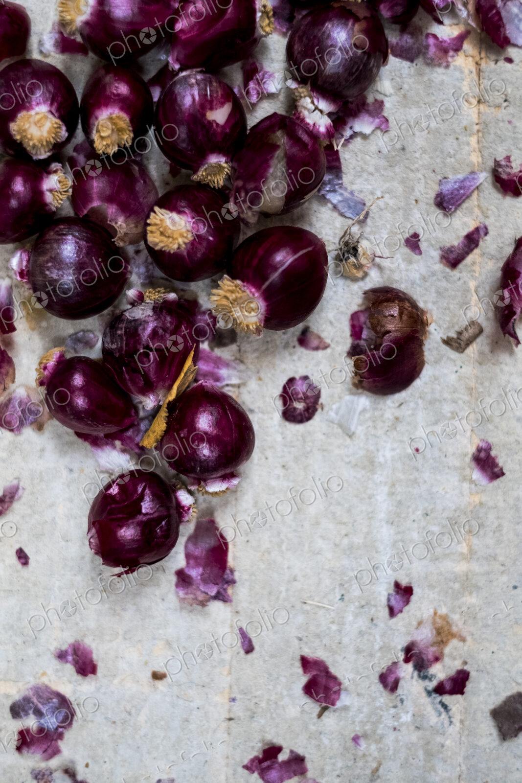 Small glossy red onions and papery outer skins on grey background.