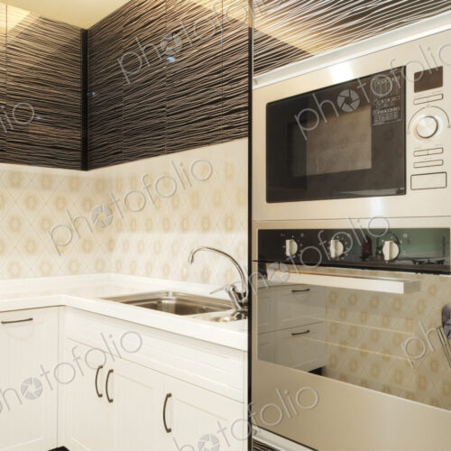 Small modern kitchen with fitted microwave oven, white cupboards and patterned tiles.