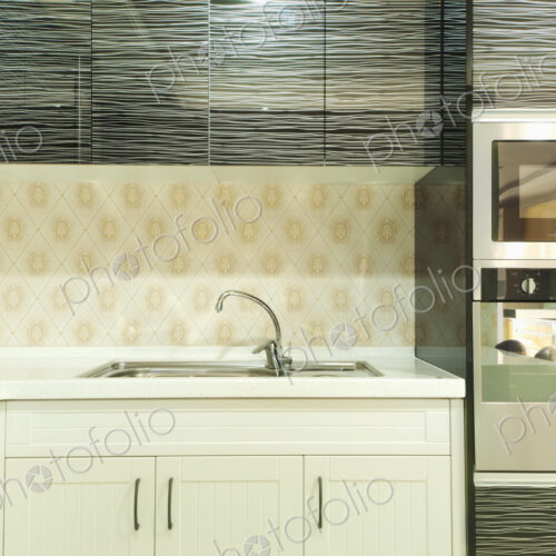 Small modern kitchen with fitted microwave oven , white cupboards and patterned tiles.