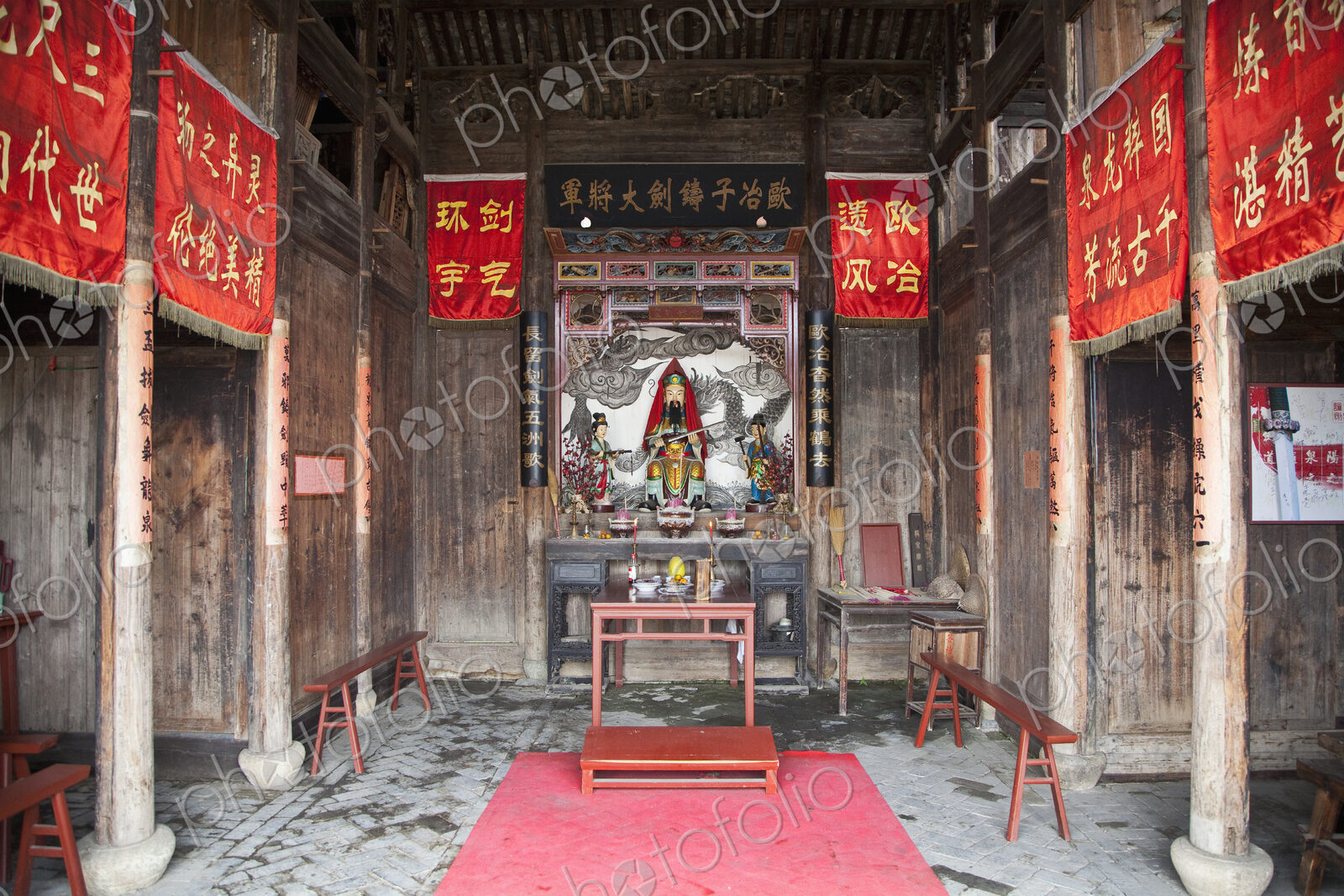 Small temple in Asia, red banners, altar with statues, incense burners