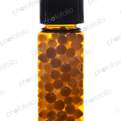 Small vial or container filled with homeopathic pills against a white background. Small vial or container filled with homeopathic pills against a white background.