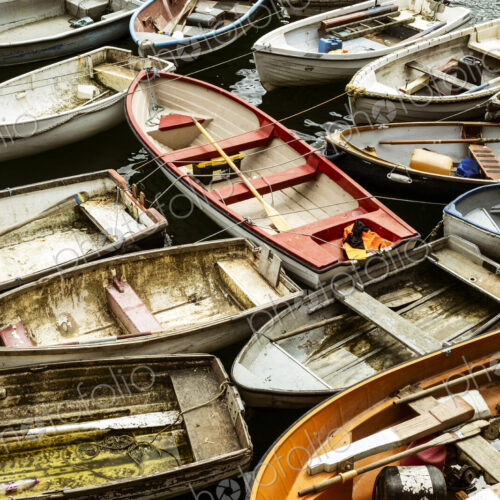 Small wooden rowing boats moored on long lines in a harbour, packed together.