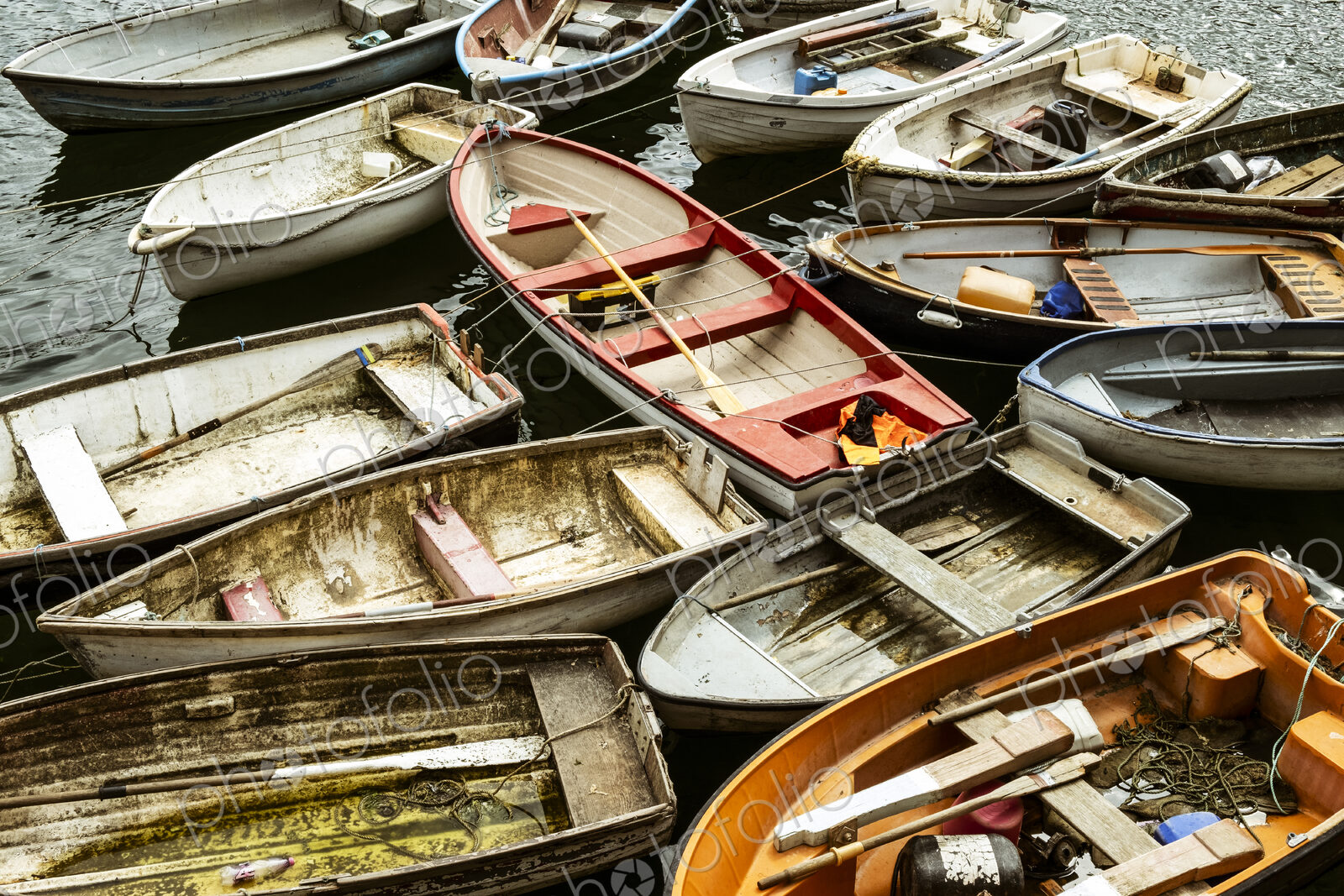 Small wooden rowing boats moored on long lines in a harbour, packed together.