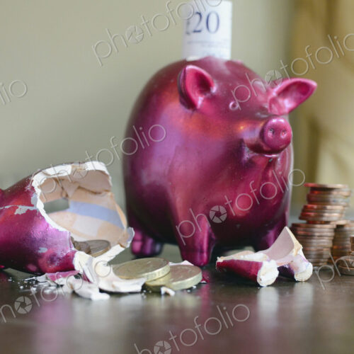 Smashed and whole piggy bank with piles of pounds on table and notes, concept of…