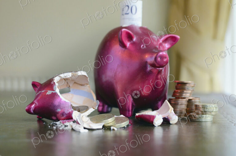 Smashed and whole piggy bank with piles of pounds on table and notes, concept of…