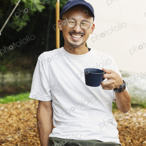 Smiling Japanese man wearing baseball cap and glasses sitting outdoors at a table,… Smiling Japanese man wearing baseball cap and glasses sitting outdoors at a table,…