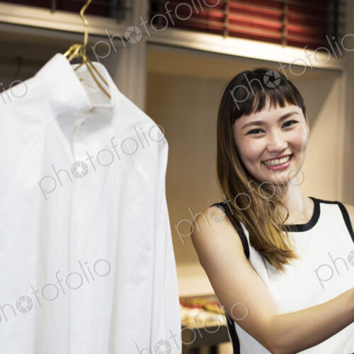 Smiling Japanese saleswoman standing in clothing store, looking at shirt. Smiling Japanese saleswoman standing in clothing store, looking at shirt.