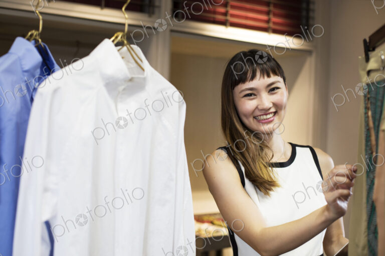 Smiling Japanese saleswoman standing in clothing store, looking at shirt.