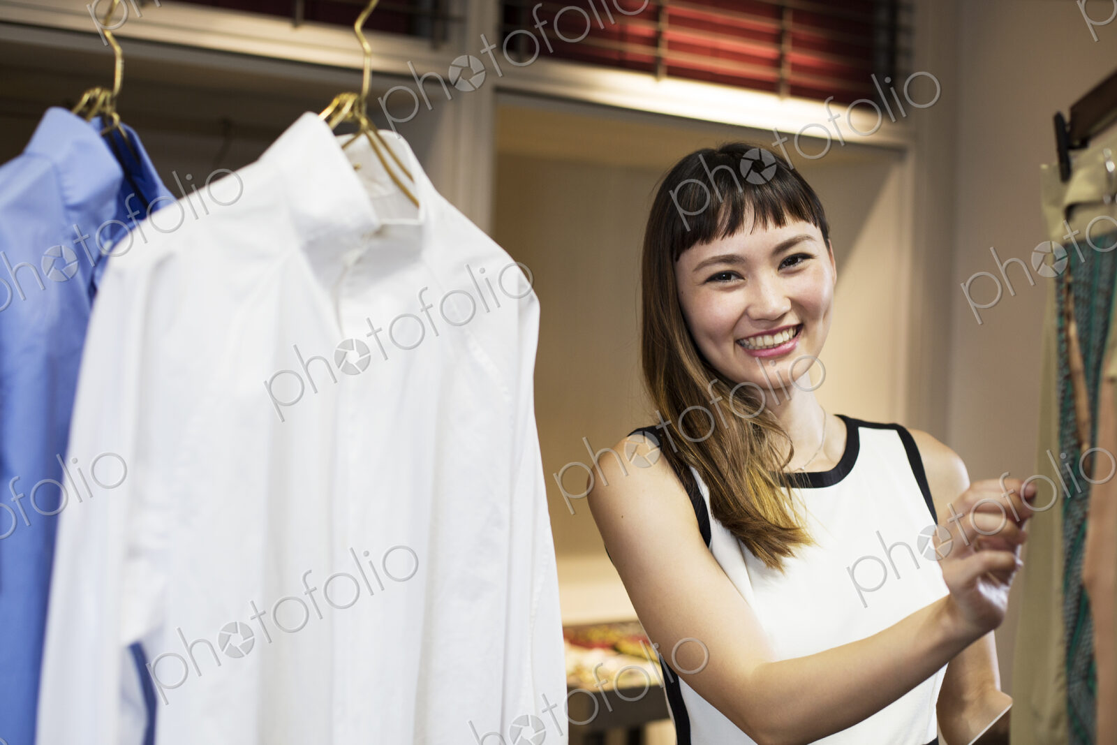 Smiling Japanese saleswoman standing in clothing store, looking at shirt.