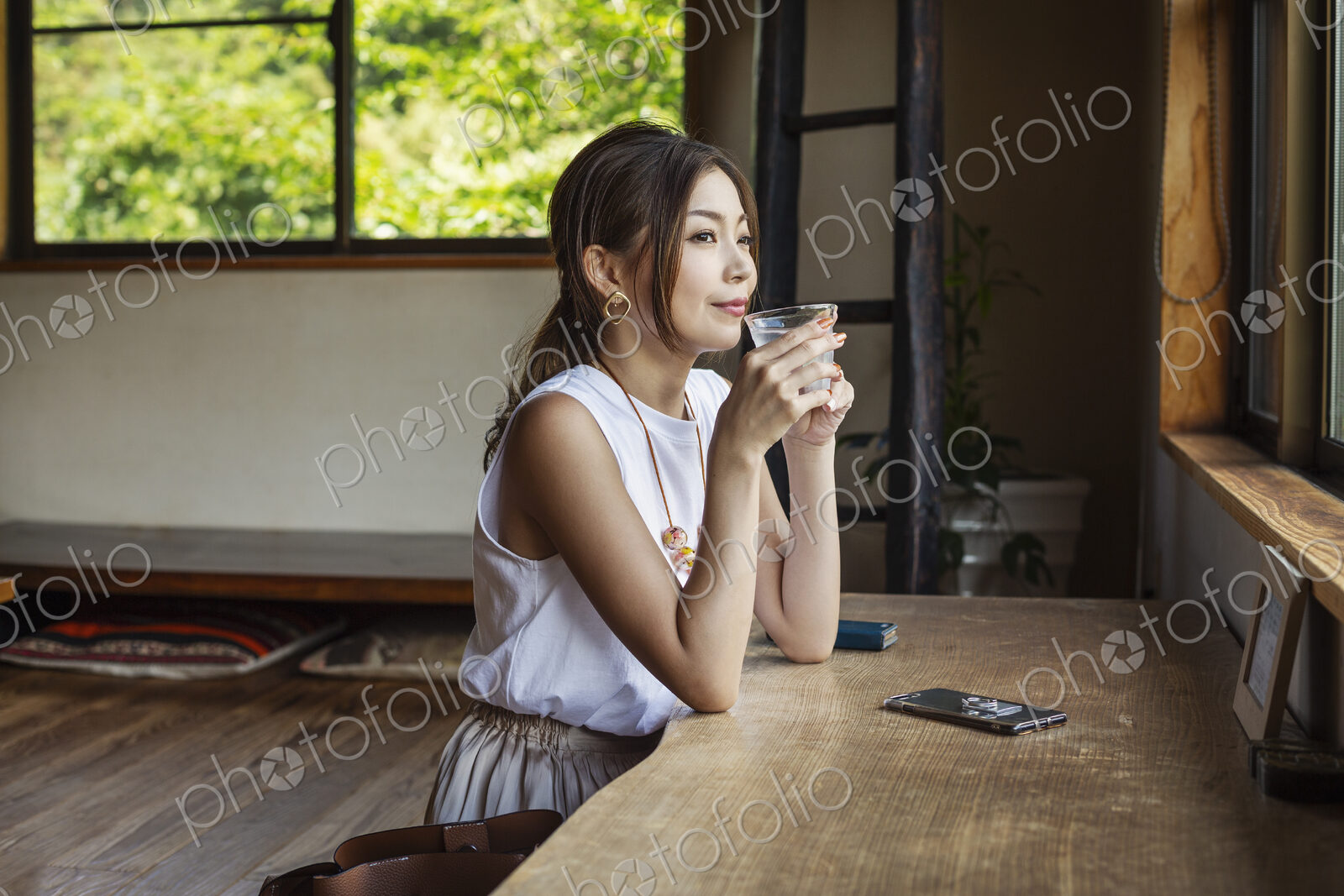 Smiling Japanese woman sitting at a table in a Japanese restaurant, drinking.