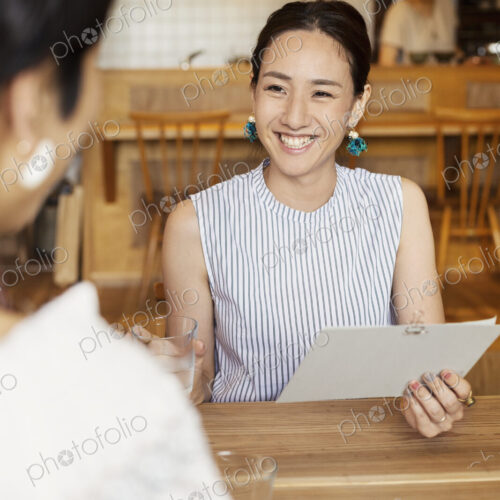 Smiling Japanese woman sitting at a table in a vegetarian cafe, holding menu. Smiling Japanese woman sitting at a table in a vegetarian cafe, holding menu.