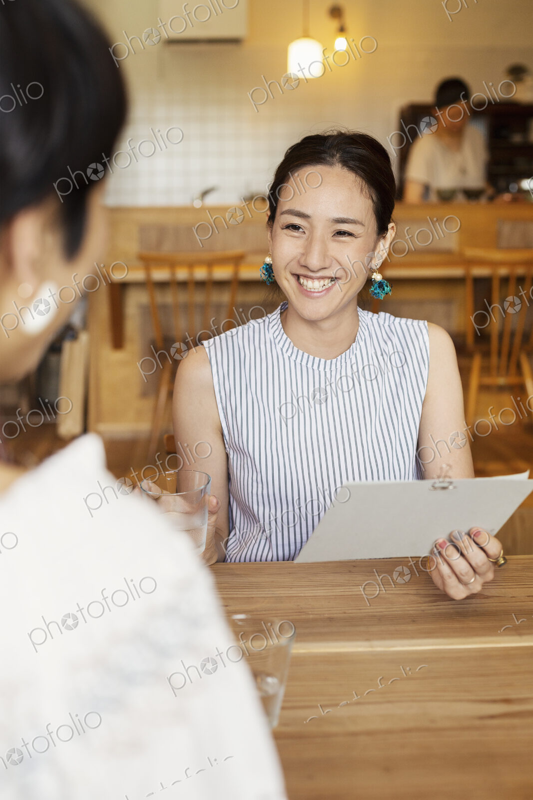 Smiling Japanese woman sitting at a table in a vegetarian cafe, holding menu.