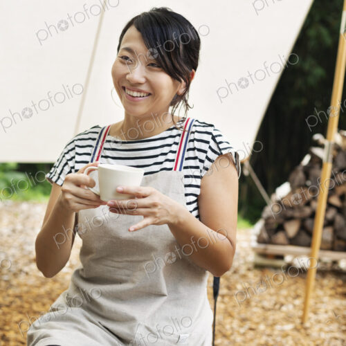Smiling Japanese woman sitting outdoors at a table, drinking cup of coffee. Smiling Japanese woman sitting outdoors at a table, drinking cup of coffee.
