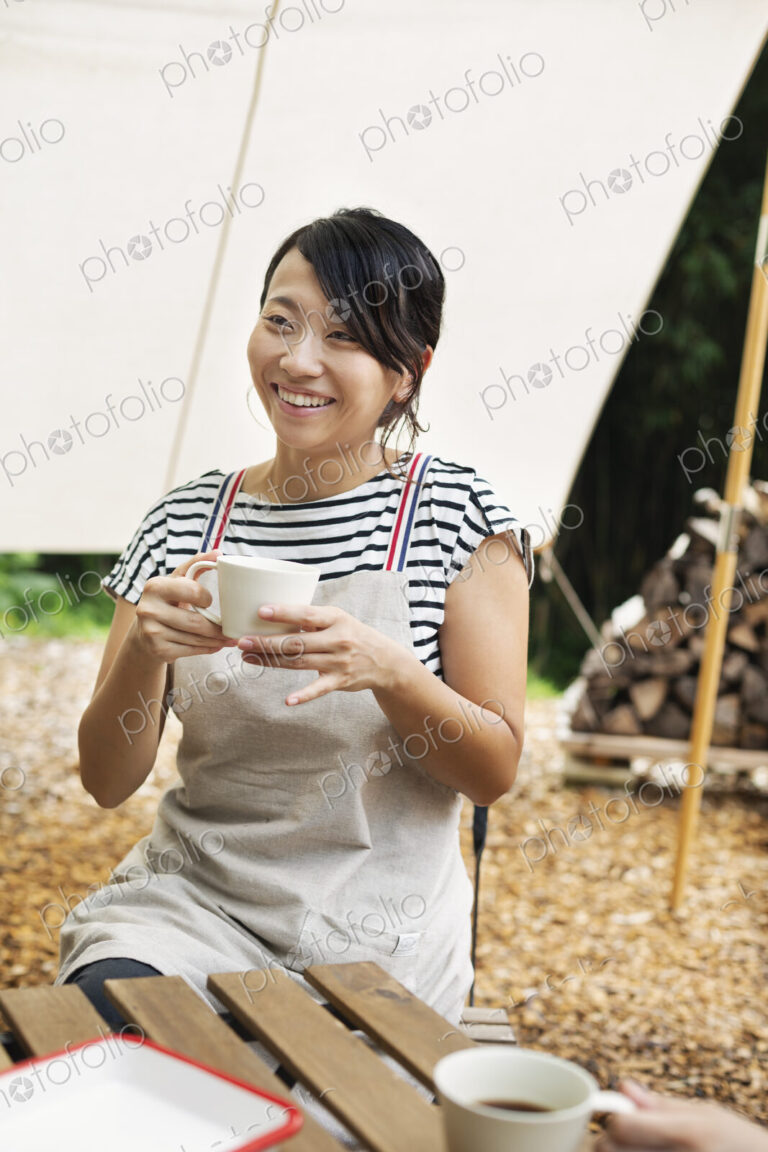 Smiling Japanese woman sitting outdoors at a table, drinking cup of coffee.