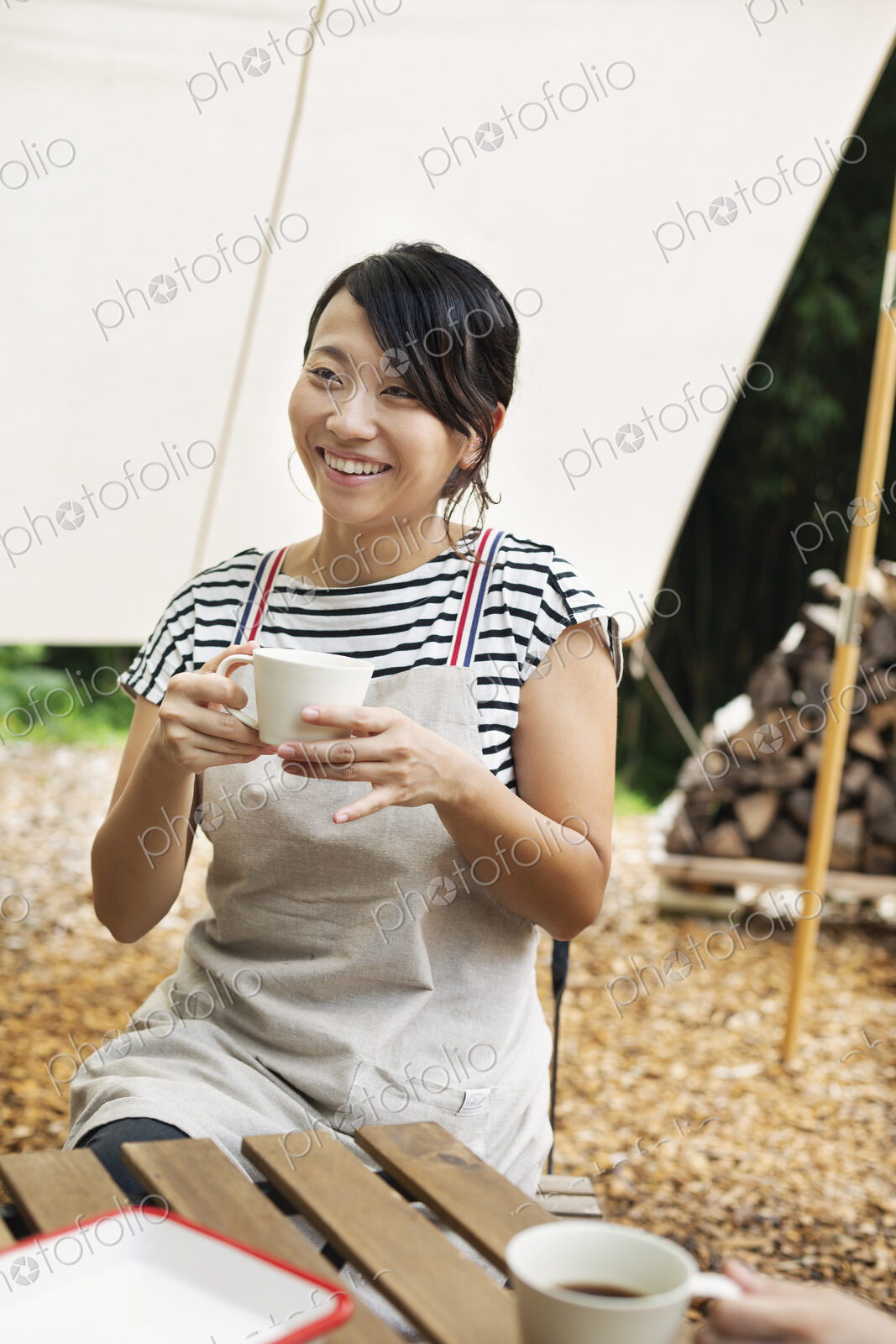 Smiling Japanese woman sitting outdoors at a table, drinking cup of coffee.
