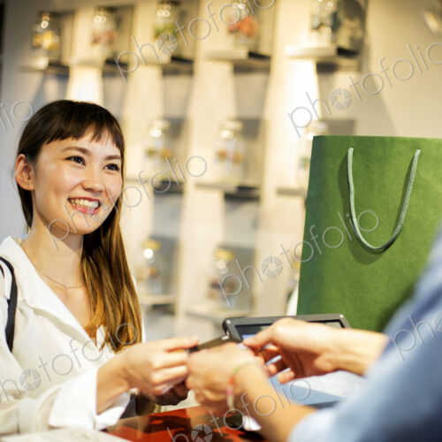 Smiling Japanese woman standing at counter in clothing store, paying with credit card.