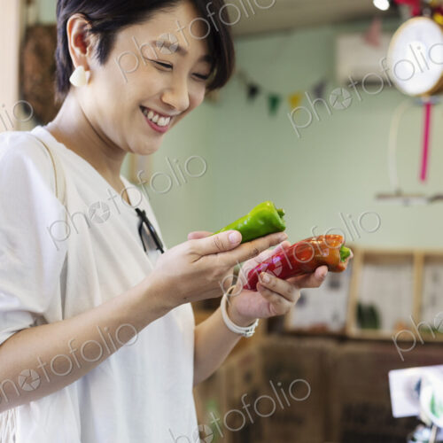 Smiling Japanese woman standing in a farm shop, holding vegetables. Smiling Japanese woman standing in a farm shop, holding vegetables.