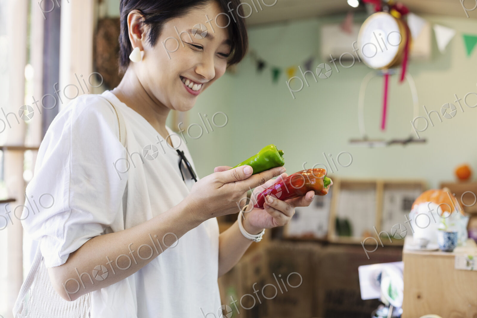Smiling Japanese woman standing in a farm shop, holding vegetables.