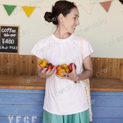 Smiling Japanese woman standing in a farm shop, holding vegetables. Smiling Japanese woman standing in a farm shop, holding vegetables.